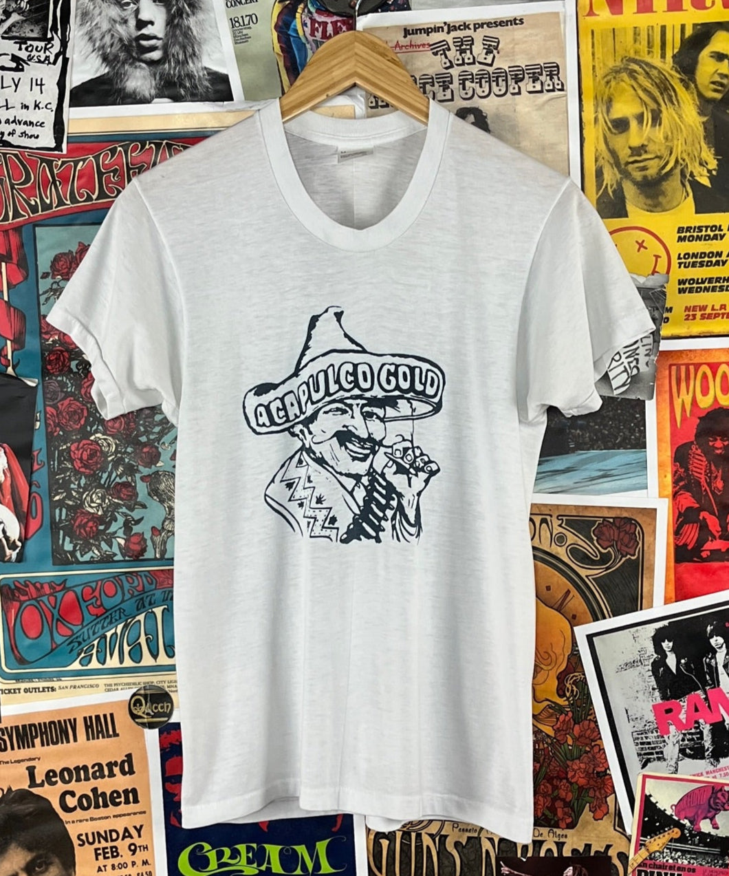 Vintage unisex 80s white and navy blue threadbare short sleeve single stitch Acapulco Gold Hispanic man pot smoking marijuana cannabis headshop graphic crewneck t-shirt. Tagged men's size medium. We estimate it to fit an adult size small. Has a few tiny holes, a fabric thread run, and a tiny spot.