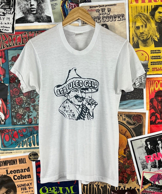 Vintage unisex 80s white and navy blue threadbare short sleeve single stitch Acapulco Gold Hispanic man pot smoking marijuana cannabis headshop graphic crewneck t-shirt. Tagged men's size medium. We estimate it to fit an adult size small. Has a few tiny holes, a fabric thread run, and a tiny spot.