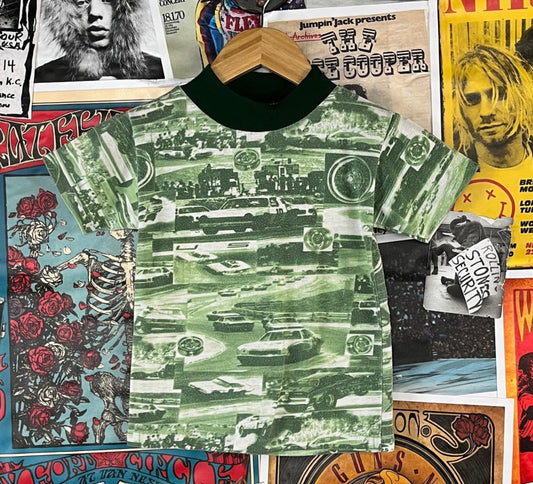Retro vintage kids boys unisex 1970s green short sleeve racecar automotive NASCAR all over print graphic mock neck pullover t-shirt top by Abels. Tagged boys size 8. We estimate it to fit kids size 6, ages 5-6. Has piling through out, but is in otherwise good, pre-owned condition. Perfect for your little racing car fan!