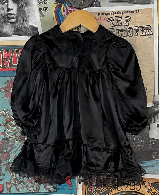 Vintage baby girls kids retro 1970s-80s solid plain black long balloon sleeve frilly satin dress. Features a lace trim collar, hem, and elastic sleeve cuffs, as well as a rhinestone button on the front. Buttons at the back collar. Adorable whimsigoth, witchy vibes! The back lace collar is a little pulled from the edge. It appears this piece was handmade. There is no listed size. We estimate it to fit size 12 months.