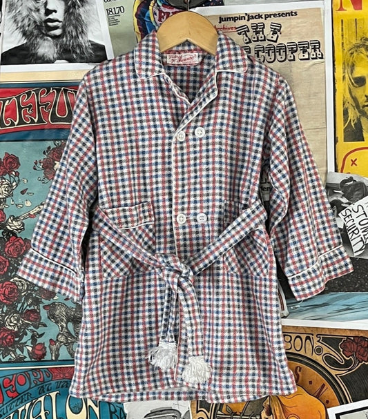 Adorable vintage boys kids retro 1950s white, blue, red, and black check plaid belted double breasted sanforized long sleeve collared bathrobe tailored by Juranta. Tagged size 3T. Features a fringe tassel pom belt and two hand pockets. Has a few light spots, but is in otherwise great, pre-owned condition.&nbsp;