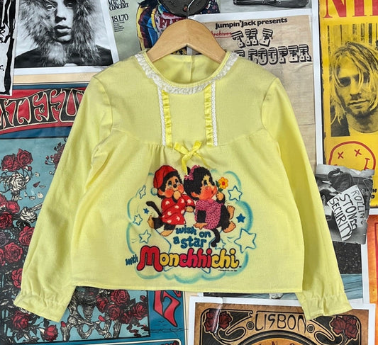 Rare vintage toddler girl kids 80s pastel yellow long sleeve Wish on a Star With Monchhichi Sekiguchi Japan cartoon graphic pajama pj shirt. Features sweet lace trimmed collar and ribbon bow detail. Buttons at the back. Had elastic sleeve cuffs, but the elasticity has worn out. There is&nbsp;also some light piling through out, and a couple of light stains at the upper back by the button.