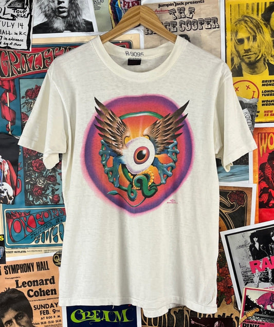 Vintage 1970s white multi-color short sleeve single stitch Stanley Mouse and Alton Kelley 'Flying Eye' art graphic print crewneck t-shirt by Heavy. Made of 100% cotton in the USA. Tagged an adult size medium. Has some minor underarm discoloration, some light yellowing and a few light stains through out. A classic tee for any rock and roll history fan!&nbsp;

It was first used on a show poster for Jimi Hendrix at the Fillmore and Winterland. The design is also associated with the Grateful Dead.